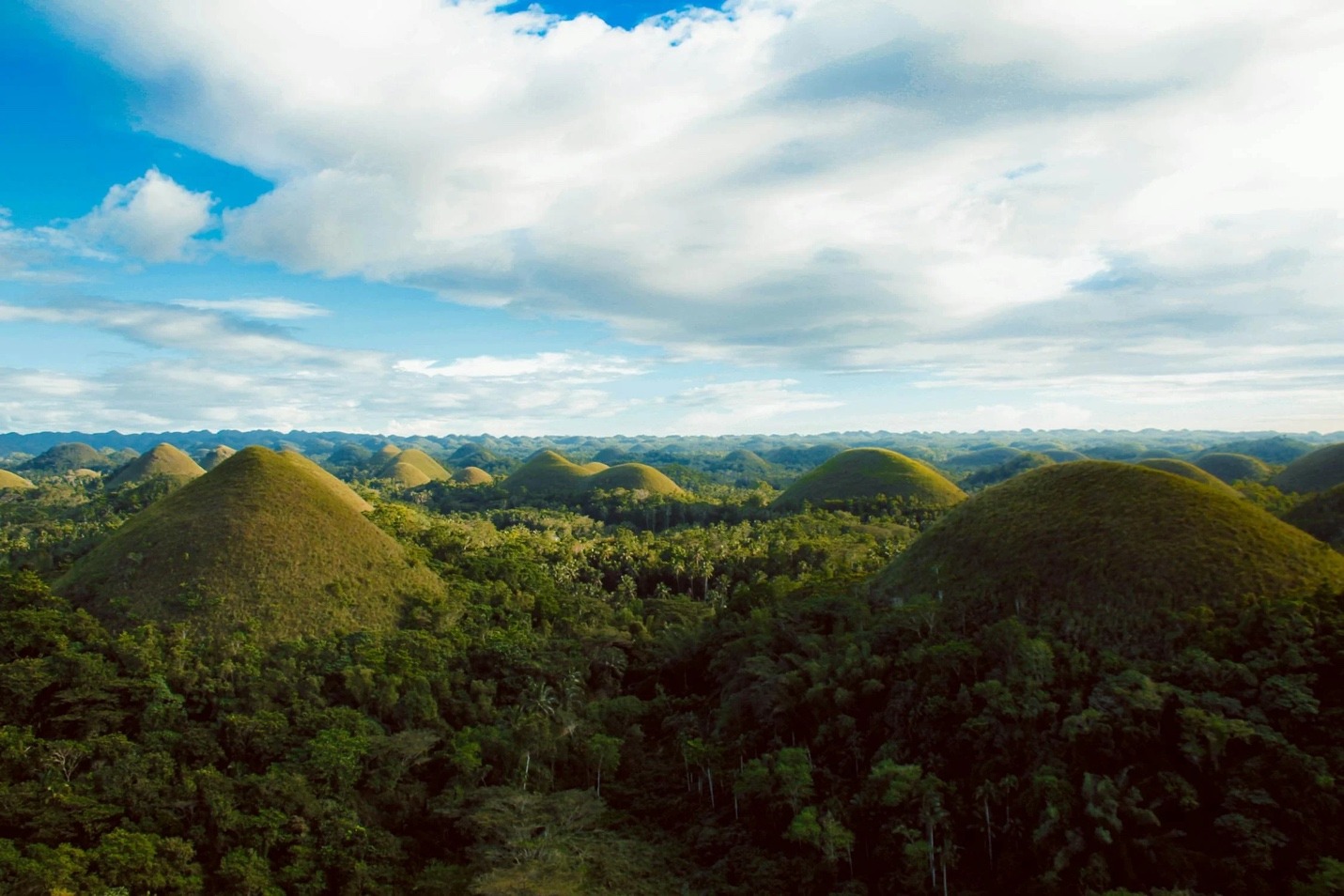 A green hills with trees and blue sky with Chocolate Hills in the background

AI-generated content may be incorrect.