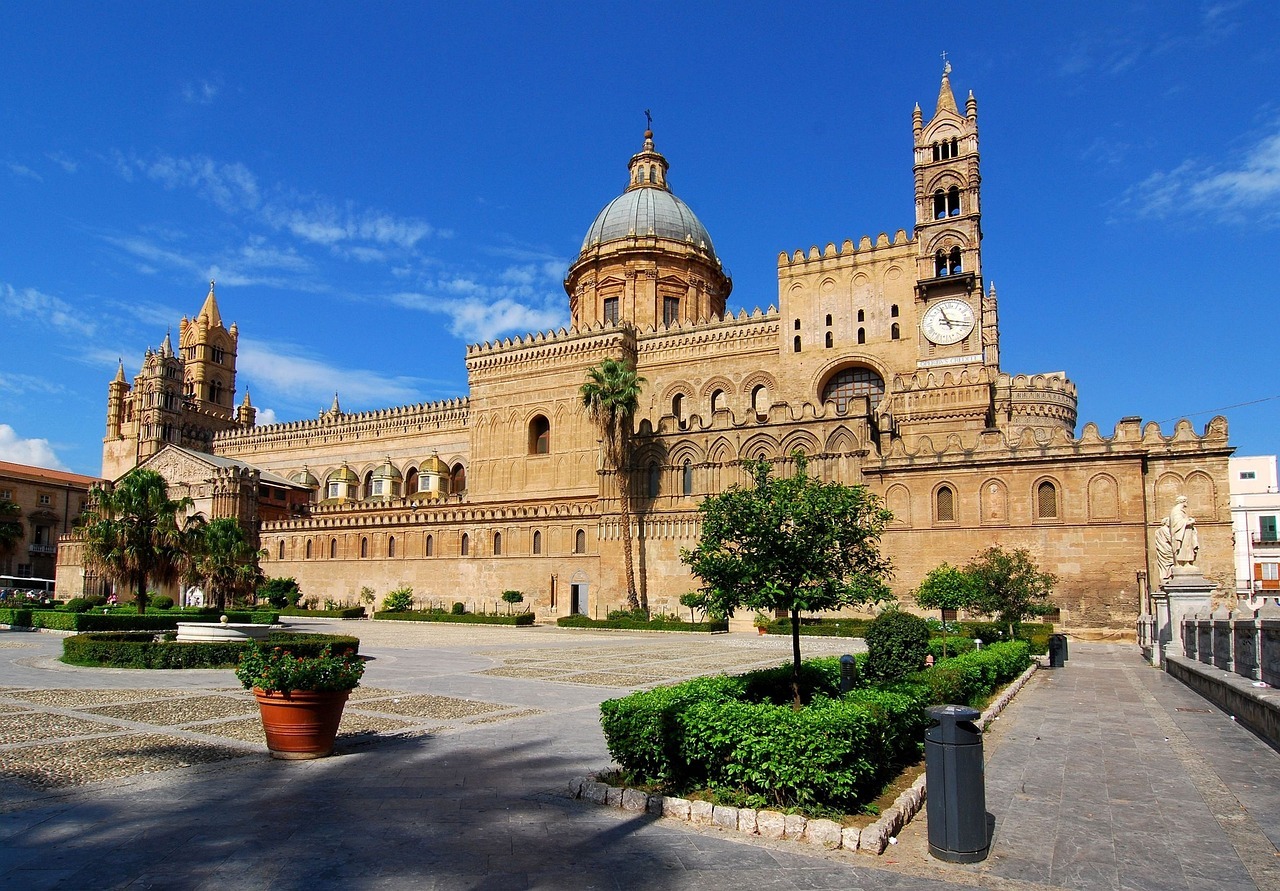A large building with a clock tower with Palermo Cathedral in the background

AI-generated content may be incorrect.